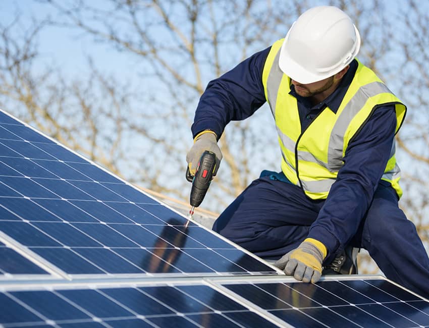 Solar installation worker in safety gear installing solar panels on a residential roof during daytime